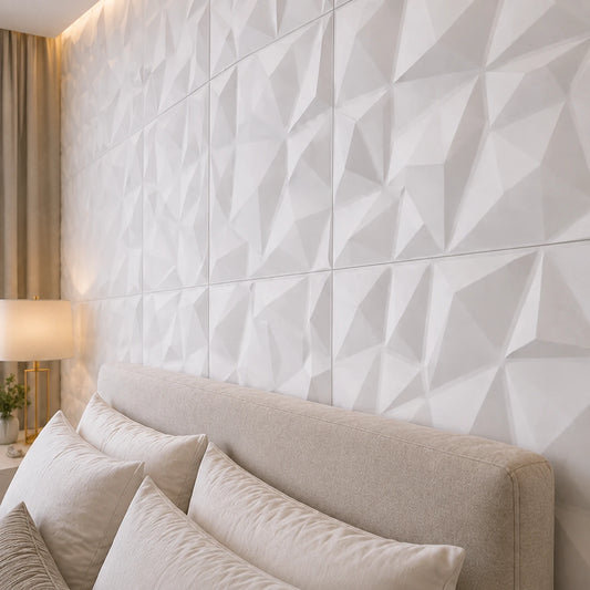 Close-up angled view of white 3D polystyrene wall panels, highlighting their faceted diamond relief, precise joints, and subtle shadows above an upholstered bed