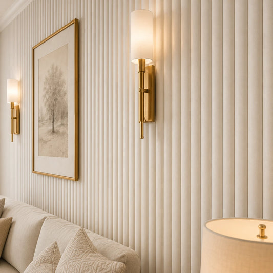 Close-up angled view of matte white fluted wall panels, showing their rounded raised profile and subtle texture, with brass sconces, framed artwork, and part of a cream sofa