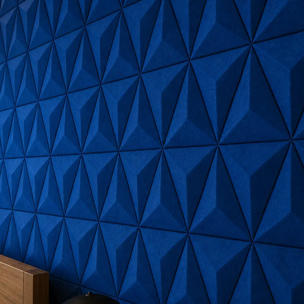 Close-up of indigo PYRAMID 3D acoustic felt wall panels, showing their sharp geometric relief, textured finish and warm ambient lighting