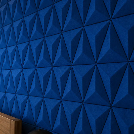 Close-up of indigo PYRAMID 3D acoustic felt wall panels, showing their sharp geometric relief, textured finish and warm ambient lighting