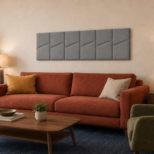 Angled living room view of six grey padded wall panels with diagonal seams mounted above a rust-coloured sofa