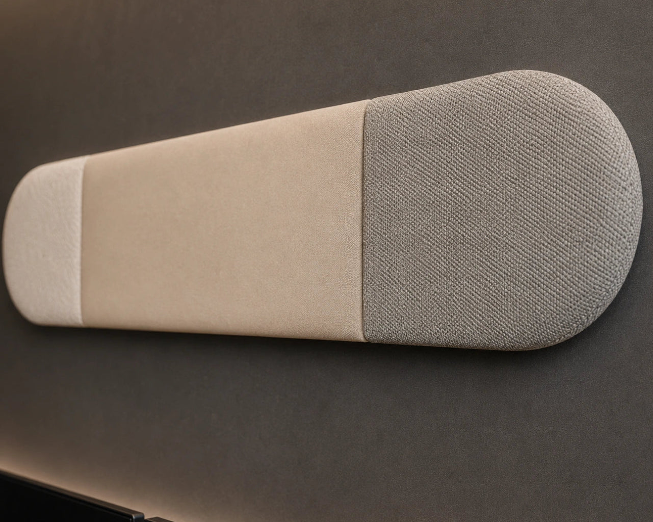Close-up angled view of a beige and grey upholstered wall panel, highlighting its rounded ends, vertical seams, padded relief and contrasting fabric textures