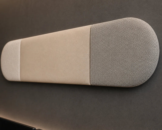 Close-up angled view of a beige and grey upholstered wall panel, highlighting its rounded ends, vertical seams, padded relief and contrasting fabric textures