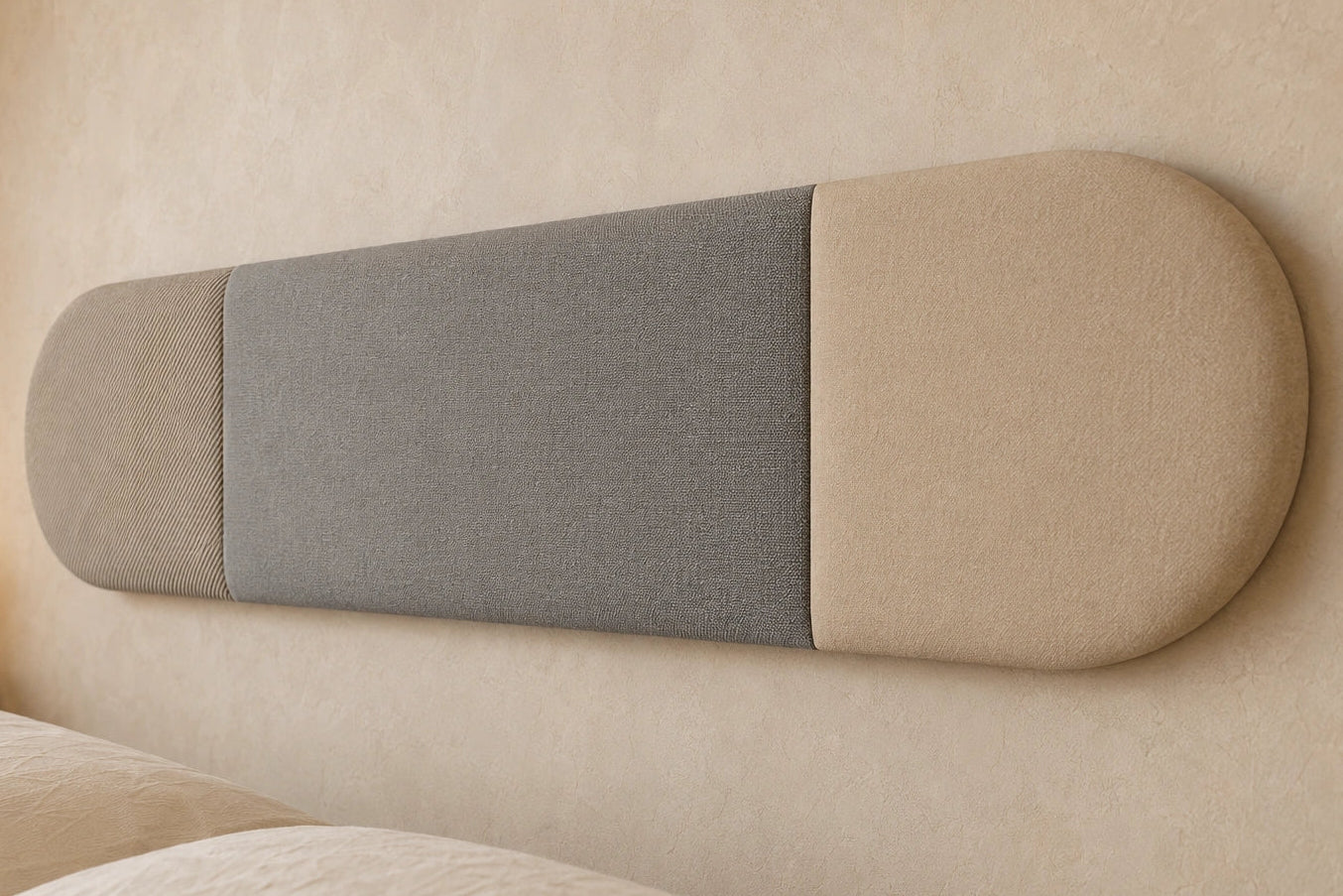 Close-up angled view of a three-section upholstered wall panel, highlighting its rounded ends, vertical seams and contrasting beige and grey fabric textures