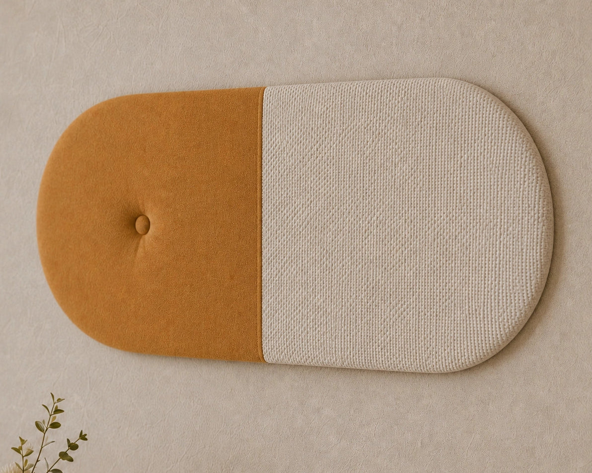 Close-up angled view of a two-tone upholstered wall panel, highlighting its mustard fabric, textured cream section, rounded shape, central seam and button detail